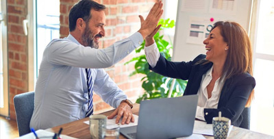 A businessman and businesswoman high-fiving each other during a business meeting, celebrating a successful collaboration.